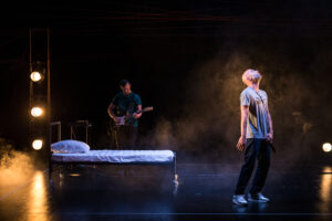 Photographie de Marc Nammour et Valentin Durup sur scène, de part et d'autre d'un lit vide. Image tirée du spectacle l'Endormi.