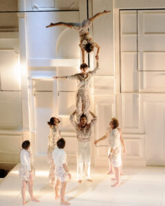 La troupe au complet est présente sur scène. Au centre, un circassien porte sur ses épaules un autre circassien qui porte sur sa tête une acrobate en grand écart