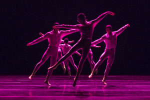 Plusieurs danseurs font des poses de danse de ballet sur scène. ils sont baignés dans une lumière rose