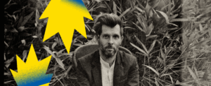 Visuel pour le concert de Hugh Coltman. Ce-dernier est assis sur un fauteuil en pleine nature, juste devant un champs de hautes herbes. Il regarde fixement la caméra. L'image est en noir et blanc.