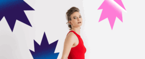 Visuel pour le concert de Nora Kamm. Nous voyons cette-dernière habillée en rouge se détachant d'un fond blanc. Elle est coiffée d'une crète blonde.