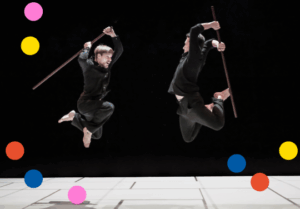 les deux interprètes en plein duel, sautant en l'air l'un vers l'autre avec des batons de combat