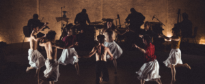 Plusieurs danseurs dansant en cercle avec en arrière plan, un groupe de musique performant en direct