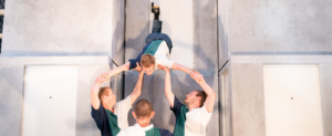 quatre acrobates v^étus du même polo à rayures, font une acrobatie. Trois porteurs portent le dernier circassien qui se retrouve dans un élan la tête en bas.
