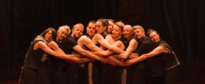 Les danseurs du spectacle sont enlacés, dans les bras les uns des autres de manière harmonieuse.