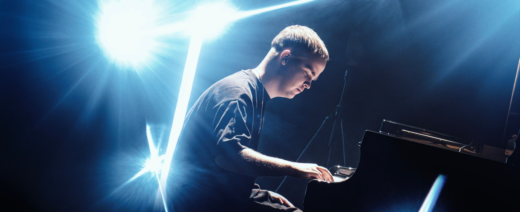 LEVI.SCT jouant du piano sur une scène éclairée de lumières de concert bleu