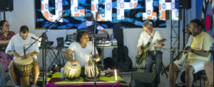 six musiciens performent sur scène avec divers instruments.